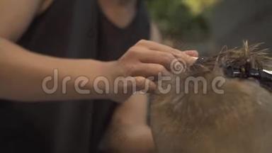 男生发型的概念。 儿童理发师在理发店用电动剃须刀给小男孩理发。 男孩